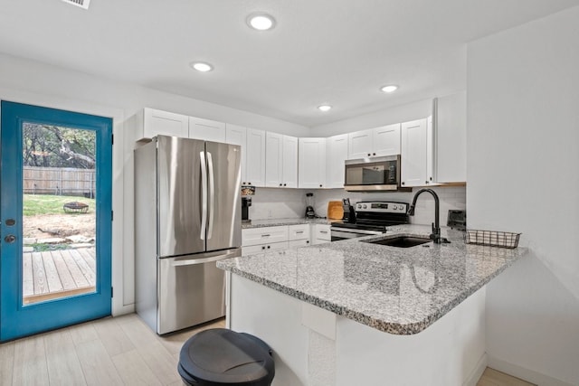 kitchen with stainless steel appliances, a peninsula, a sink, white cabinets, and light stone countertops