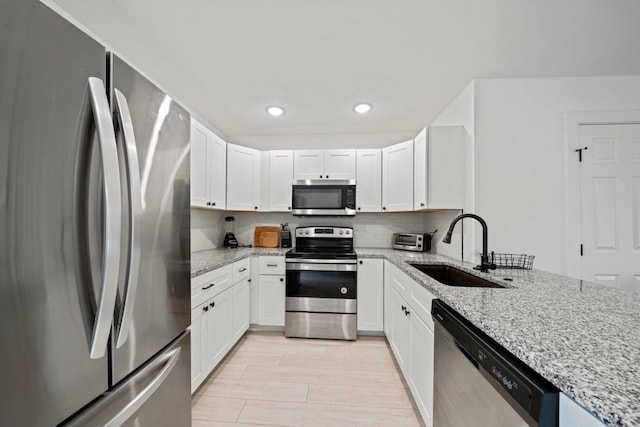 kitchen with appliances with stainless steel finishes, a sink, white cabinetry, and light stone countertops