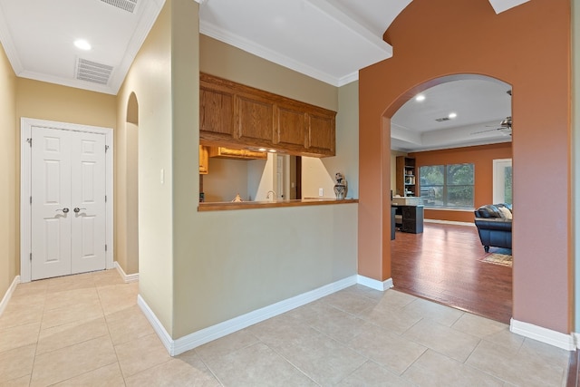 hallway with light tile patterned floors, ornamental molding, and arched walkways