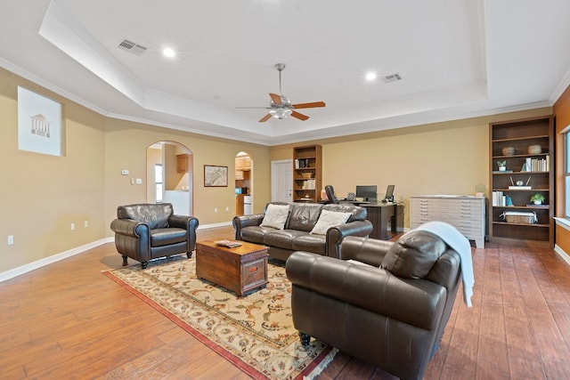 living area with visible vents, arched walkways, a raised ceiling, and wood finished floors