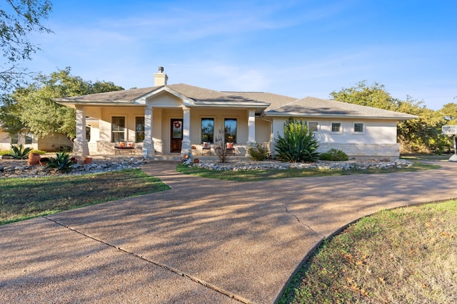 view of front facade featuring covered porch, a chimney, and stucco siding