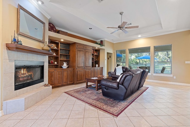 living area with a tiled fireplace, a tray ceiling, light tile patterned flooring, and crown molding