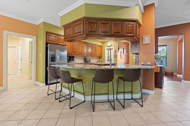 kitchen with light stone counters, brown cabinets, light tile patterned floors, stainless steel fridge with ice dispenser, and a kitchen bar