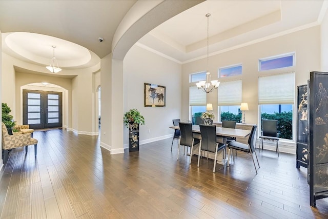 dining space featuring a tray ceiling, french doors, arched walkways, and wood finished floors