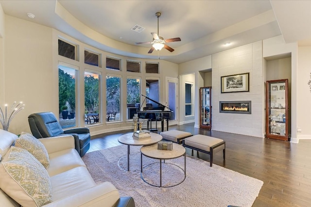 living area featuring dark wood-style floors, a raised ceiling, visible vents, a tile fireplace, and baseboards