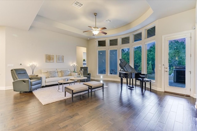 living area featuring dark wood-type flooring, a ceiling fan, visible vents, baseboards, and a tray ceiling