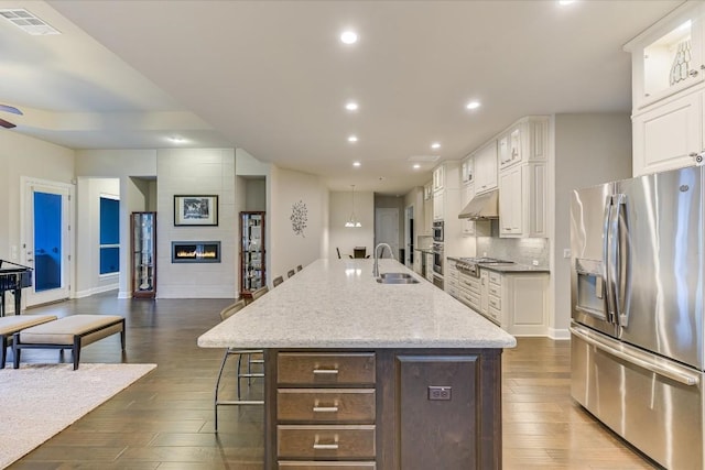 kitchen featuring appliances with stainless steel finishes, a large island with sink, under cabinet range hood, white cabinetry, and a sink