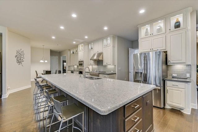 kitchen with under cabinet range hood, white cabinets, stainless steel refrigerator with ice dispenser, and a large island