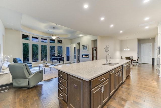 kitchen with a glass covered fireplace, wood finished floors, a kitchen island with sink, stainless steel dishwasher, and a sink