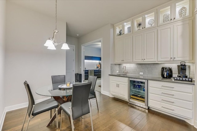 kitchen featuring beverage cooler, a sink, hanging light fixtures, dark countertops, and glass insert cabinets