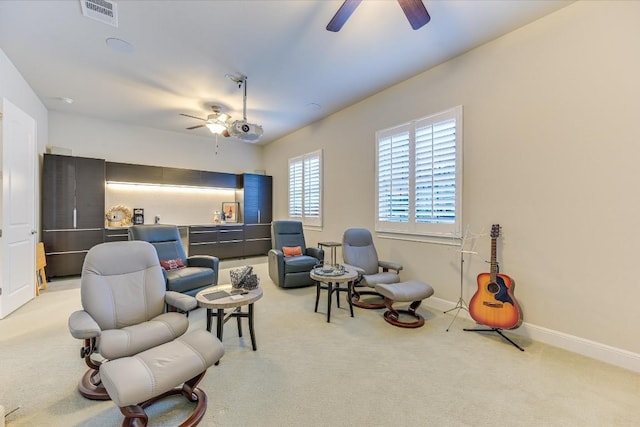 living area with baseboards, visible vents, a ceiling fan, and light colored carpet