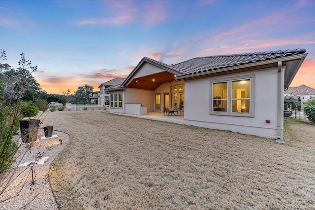 rear view of house with a tile roof, a patio, fence, and stucco siding