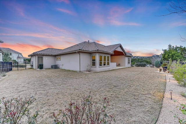 back of property at dusk with central air condition unit, a tiled roof, fence, and stucco siding