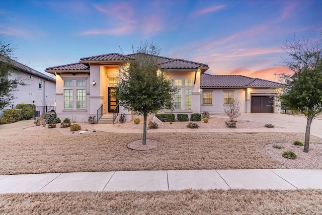 mediterranean / spanish-style home with a garage, concrete driveway, a tiled roof, and stucco siding