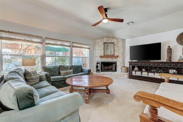 carpeted living area with lofted ceiling, ceiling fan, visible vents, and a stone fireplace