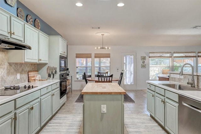 kitchen featuring a kitchen island, a sink, hanging light fixtures, wooden counters, and black appliances