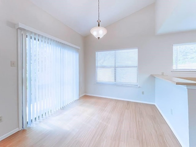 spare room featuring lofted ceiling, light wood-type flooring, and baseboards