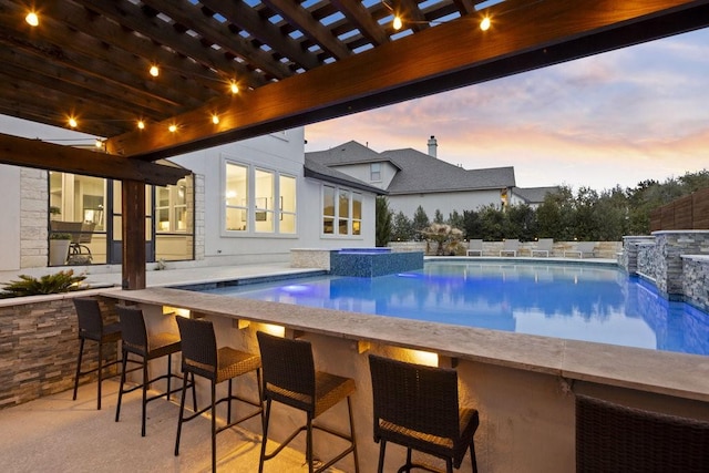 pool at dusk featuring an outdoor bar, a pool with connected hot tub, and a pergola