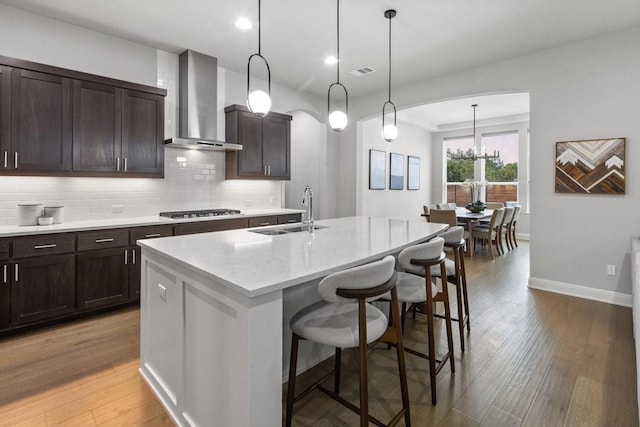 kitchen featuring wall chimney range hood, a center island with sink, pendant lighting, and a sink