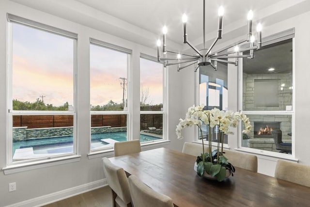 dining area with a notable chandelier, baseboards, wood finished floors, and a stone fireplace