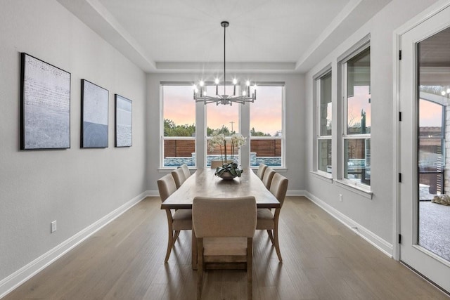 dining space with light wood finished floors, baseboards, a raised ceiling, and a notable chandelier