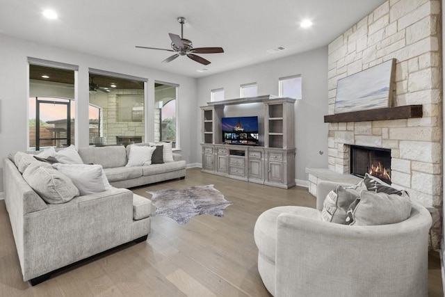 living area with baseboards, visible vents, a ceiling fan, a stone fireplace, and light wood-type flooring