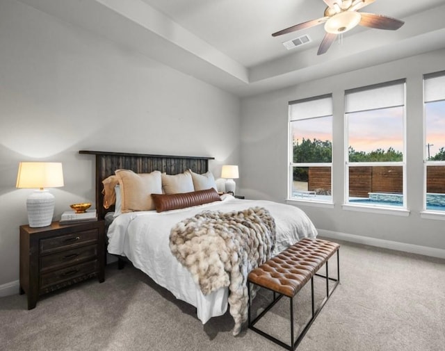 carpeted bedroom with a ceiling fan, a raised ceiling, visible vents, and baseboards