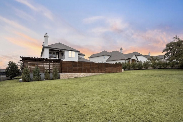 yard at dusk featuring fence and a pergola