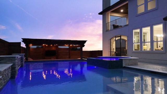 pool at dusk with fence and a pool with connected hot tub