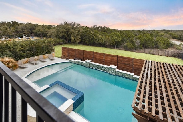 pool at dusk featuring a lawn, a fenced backyard, and a pool with connected hot tub