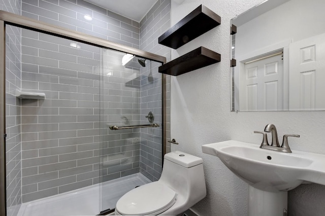 bathroom featuring a sink, a textured wall, a shower stall, and toilet