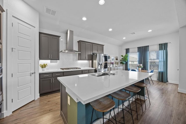 kitchen with visible vents, a sink, wall chimney range hood, an island with sink, and a kitchen bar