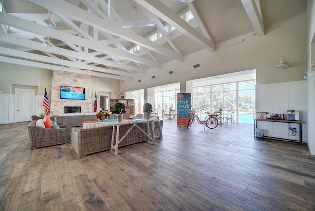 living room featuring visible vents, beamed ceiling, a stone fireplace, and wood finished floors