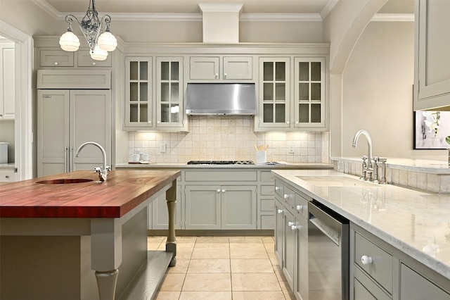 kitchen featuring stainless steel dishwasher, butcher block countertops, a sink, and under cabinet range hood