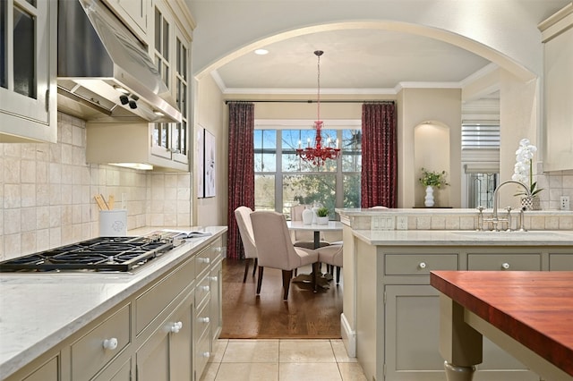 kitchen with decorative light fixtures, stainless steel gas stovetop, glass insert cabinets, a sink, and under cabinet range hood