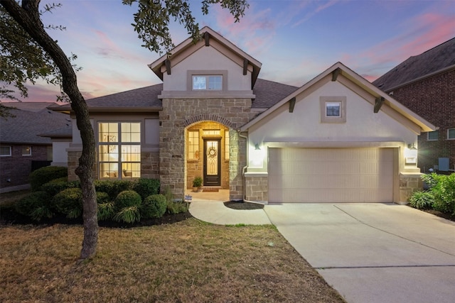 traditional home with driveway, stone siding, a garage, and stucco siding