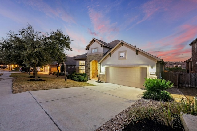 traditional home with stucco siding, fence, a garage, stone siding, and driveway