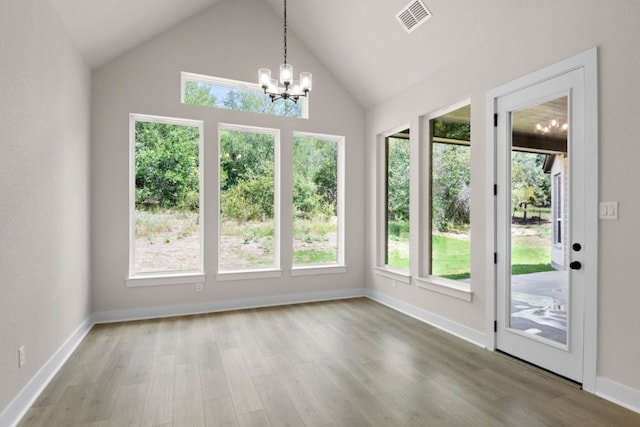 unfurnished dining area with lofted ceiling, wood finished floors, visible vents, baseboards, and an inviting chandelier