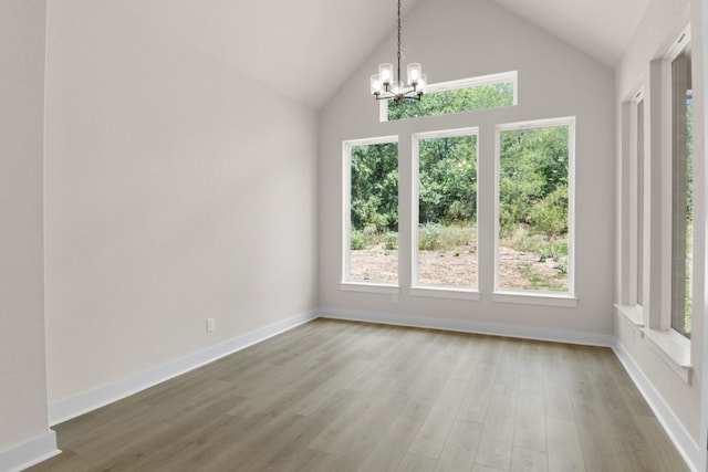 unfurnished dining area with high vaulted ceiling, a notable chandelier, baseboards, and wood finished floors