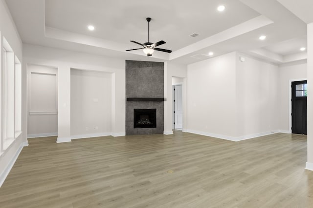 unfurnished living room featuring light wood-style floors, a tray ceiling, and a tiled fireplace