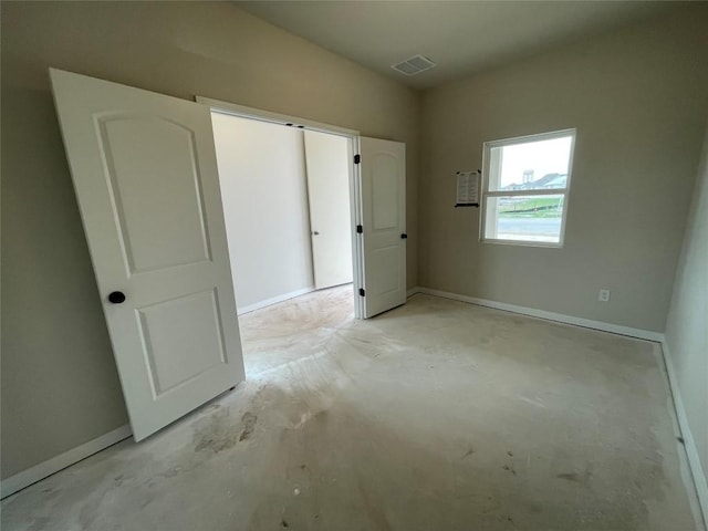 unfurnished bedroom with a closet, unfinished concrete flooring, visible vents, and baseboards