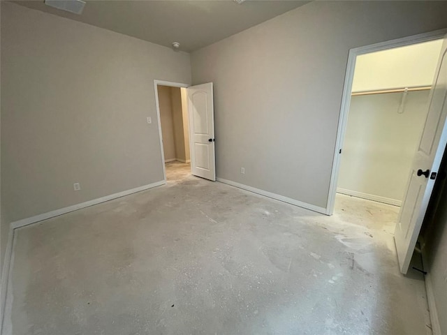 unfurnished bedroom with a closet, baseboards, a walk in closet, and unfinished concrete flooring