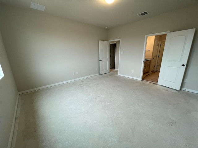 unfurnished bedroom with concrete flooring, connected bathroom, visible vents, and baseboards