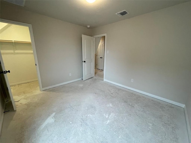 unfurnished bedroom featuring a walk in closet, a closet, visible vents, concrete flooring, and baseboards