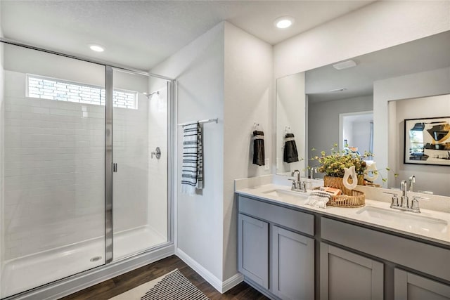 bathroom with double vanity, wood finished floors, a stall shower, and a sink