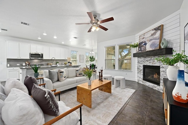 living area featuring dark tile patterned floors, a fireplace, visible vents, and a ceiling fan