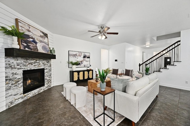 living area with stairs, a stone fireplace, a ceiling fan, and baseboards