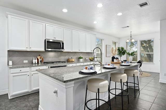 kitchen with stainless steel appliances, an island with sink, visible vents, and white cabinets