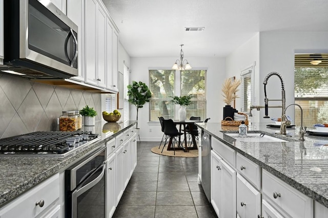 kitchen with stainless steel appliances, hanging light fixtures, stone countertops, white cabinetry, and a sink