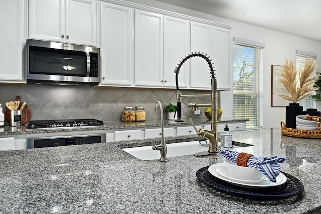 kitchen with white cabinets, stone counters, stainless steel appliances, and backsplash